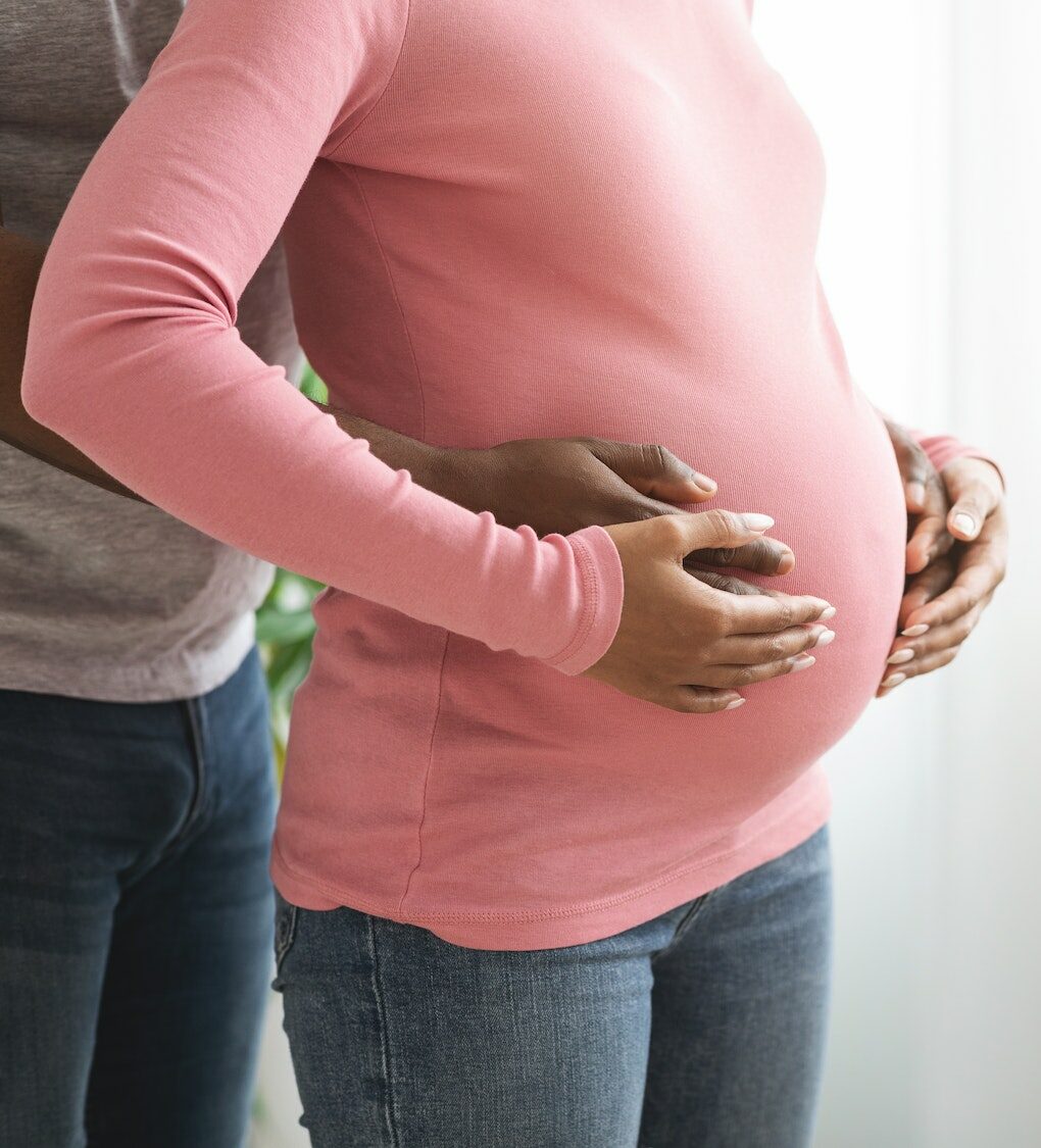 Closeup of african pregnant couple hug, standing next to window